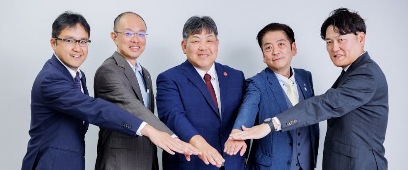 写真：令和7年度支援先企業の皆さんが笑顔で手を組むようす